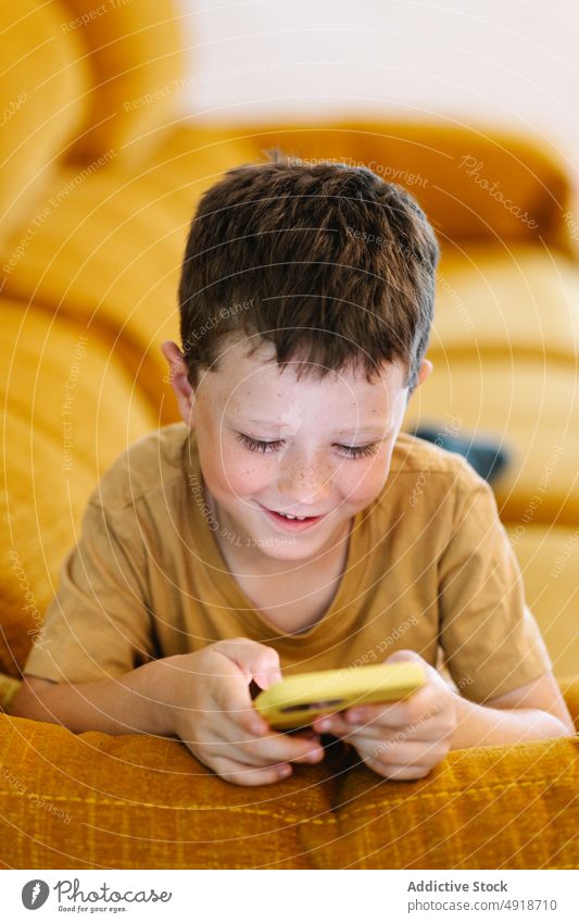 Glücklicher Junge auf einem Sofa liegend, der auf seinem Smartphone surft Kind heimwärts Telefon Browsen Lächeln Freude Technik & Technologie im Innenbereich