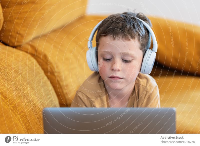 Junge auf einem Sofa liegend, mit Kopfhörern auf dem Kopf und mit einem Laptop Kind Computer Kaukasier Technik & Technologie männlich ernst Konzentration