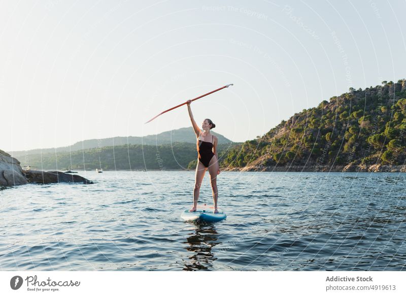 Frau in Badekleidung schwimmt auf Paddleboard Paddelbrett sportlich Surfer Hobby See Wasser Reihe üben Schwimmer Baum Küste Gerät Zusatzplatine Abenteuer