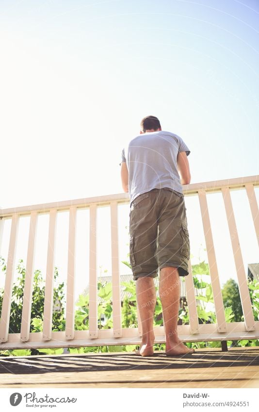 Mann steht im Sommer auf einem Balkon und genießt das schöne Wetter Sonnenschein Garten Haus beobachten Überblick Schönes Wetter