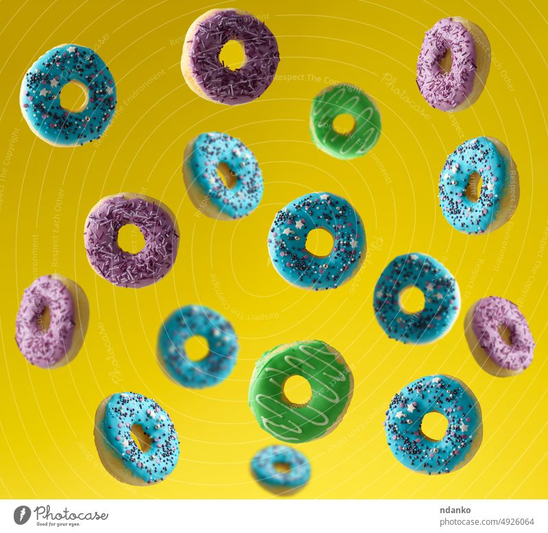 Mehrfarbige Donuts mit Zuckerstreuseln bestreut fliegen auf einem gelben Hintergrund Krapfen Teigwaren Doughnut fallend Fliege Lebensmittel gefrostet Glasur