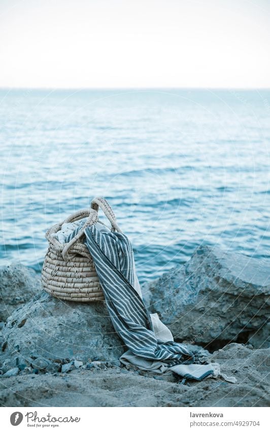 Ein Strohkorb, ein Peshtemal-Baumwollhandtuch, das auf den Felsen eines wilden Strandes liegt, blau Feiertag Meer Wasser Korb Klippe wolkenlos Küstenlinie