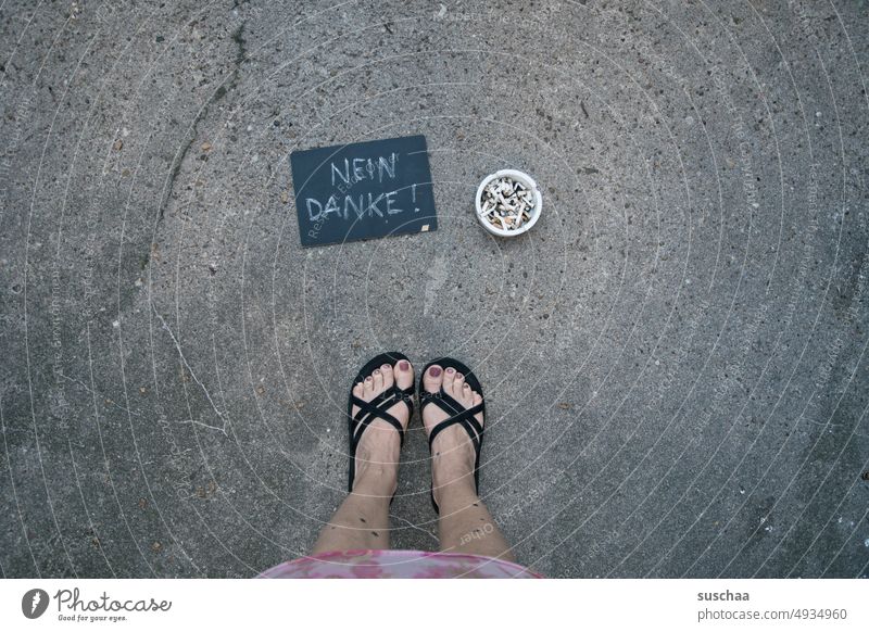 frau steht neben einem gefüllten aschenbecher mit tafel, auf der geschrieben steht " nein danke!" Füße Beine weiblich Flipflops Sommer Straße Asphalt