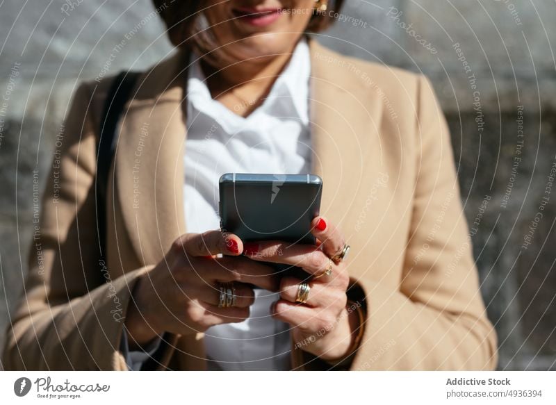 Zufriedene Frau benutzt Smartphone auf der Straße Texten Lächeln benutzend Stil sonnenbeschienen tagsüber Browsen Textnachricht Mobile Telefon Funktelefon