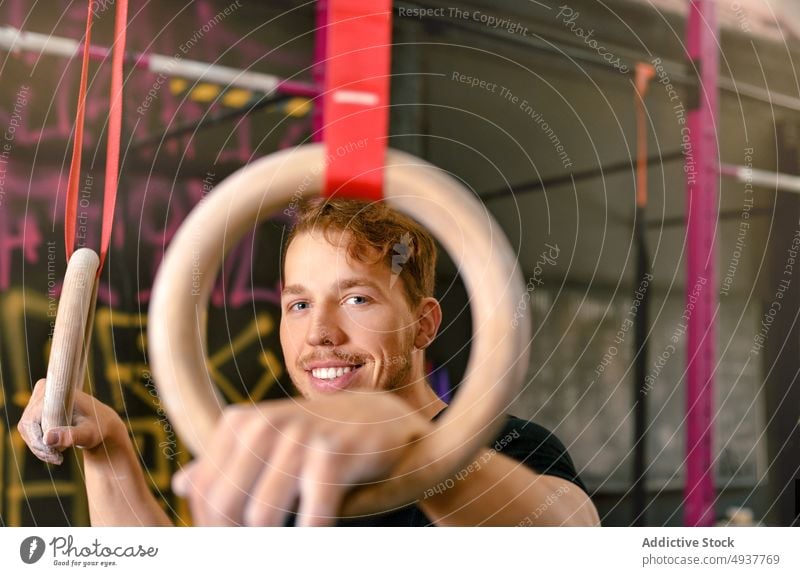 Männlicher Athlet, der sich auf eine Übung mit Gymnastikringen vorbereitet Sportler Ring gymnastisch Lächeln vorbereiten Training Fitnessstudio Glück stark