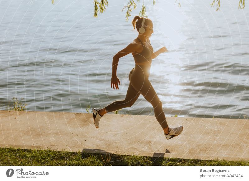 Aktive junge schöne Frau läuft auf der Promenade am Flussufer entlang aktiv Aktivität Athlet sportlich Großstadt Ausdauer Übung Fitness Kopfhörer Headset