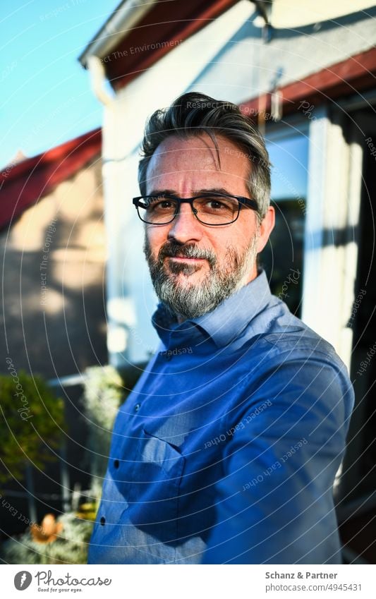 Mann mit Bart und Brille blickt selbstsicher selfie Portrait Hemd ernst schmunzeln hartes Licht Schatten Außenaufnahme Selbstportrait Blick in die Kamera