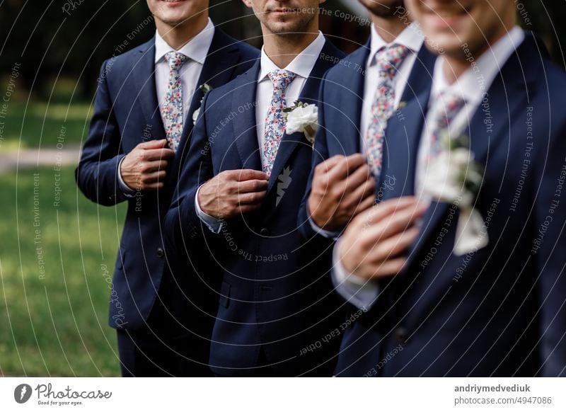 eleganter Bräutigam Männer mit stilvollen Blumen Krawatte. weiße Blumen im Knopfloch, sind die Männer des Bräutigams in einem dunklen Anzug gekleidet. Hochzeitstag. Outfit des Tages.