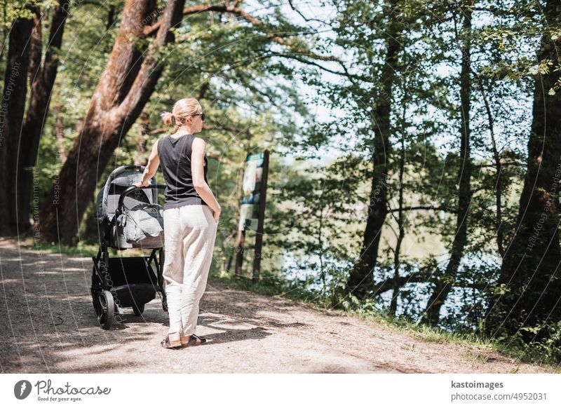 Rückansicht einer lässig gekleideten Mutter, die mit einem Kinderwagen im Stadtpark spazieren geht. Familie, Kind und Elternschaft Konzept. Mutterschaft