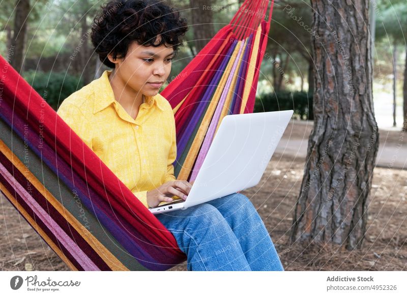 Ethnische Frau mit Laptop in der Hängematte Teenager Park benutzend ruhen Sommer sich[Akk] entspannen Anschluss Surfen lässig nachdenklich genießen Erholung