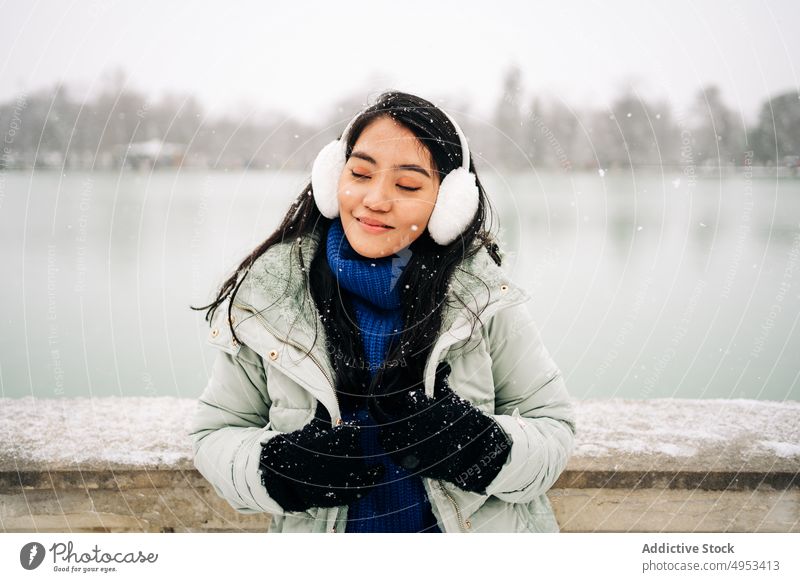 Asiatische Frau unter dem Schnee in der Nähe des Sees im Winter Schneeflocke bewundern Winterzeit Fluss idyllisch Stauanlage urban Porträt Zaun alt Stil