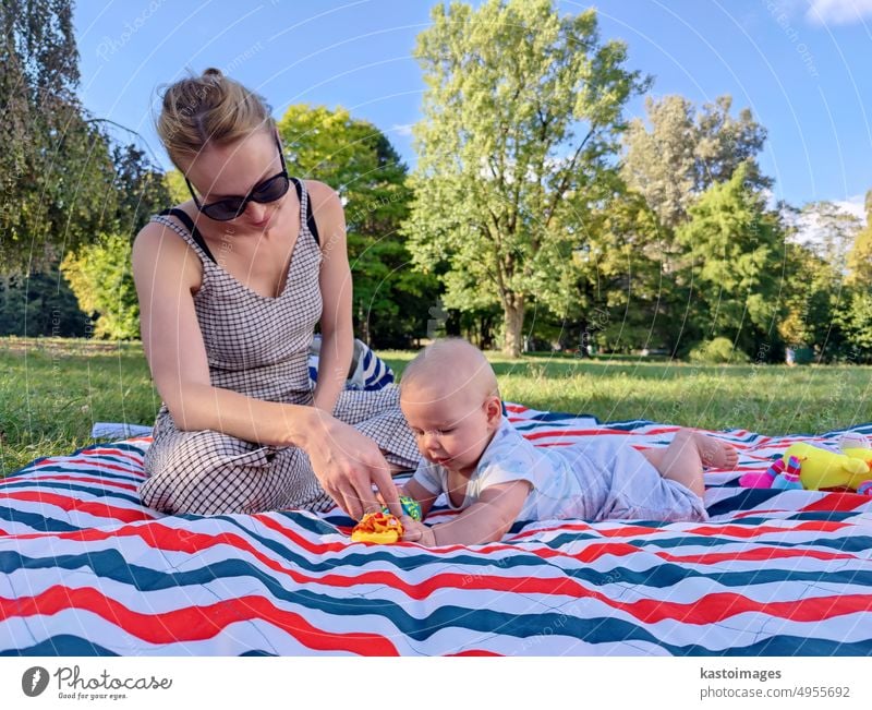 Moderne trendige Mutter, die mit ihrem kleinen Jungen auf einer Matte auf einer Wiese im Freien im öffentlichen Stadtpark spielt Mama Baby Mutterschaft Kindheit