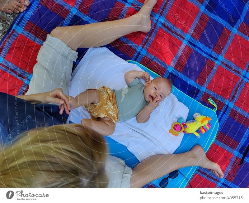 Moderne trendige Mutter, die mit ihrem kleinen Jungen auf einer Matte auf einer Wiese im Freien im öffentlichen Stadtpark spielt Mama Baby Mutterschaft Kindheit