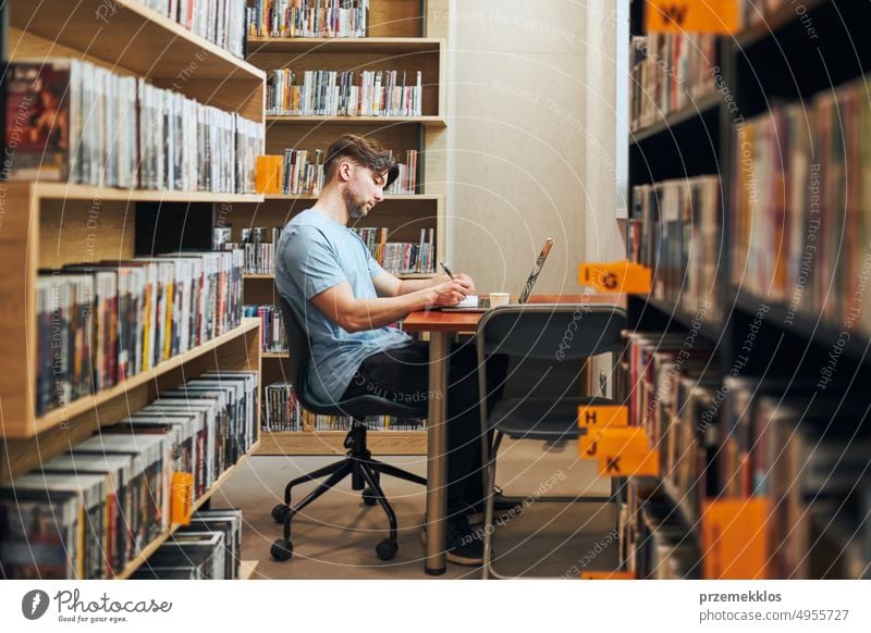 Student lernt in der Bibliothek. Junger Mann bereitet sich am Laptop auf einen Test vor. Mann hört sich einen Online-Kurs an. Konzentrierter Student, der für College-Prüfungen lernt