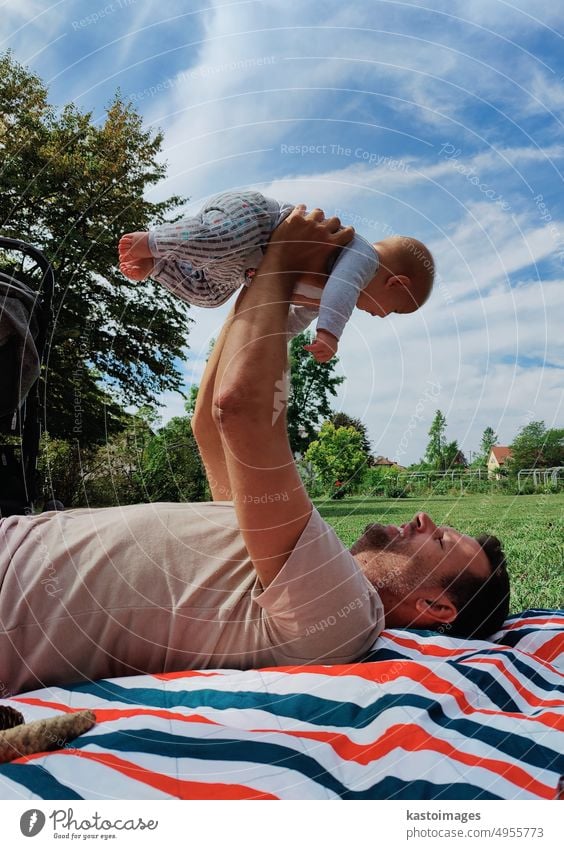 stolzer Vater hebt sein Baby hoch und spielt mit ihm auf einer Matte auf einer Wiese in einem öffentlichen Stadtpark Kindheit Lifestyle Mama Familie Brust Glück