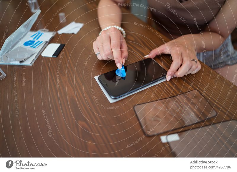 Crop-Technikerin entfernt Staub vom Smartphone-Bildschirm Frau entfernen Staubwischen Absorber Sauberkeit Klebrig Tisch Werkstatt vorbereiten Mobile Telefon