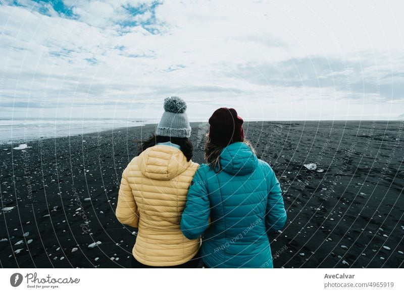 Paar weiblich in gelber Regenkleidung in den schwarzen Sand Diamant Strand in der Nähe von Jokulsarlon während eines Roadtrips Reise erkunden wilden Ländern von Island.Abenteuer Urlaub gesunden Lebensstil Rucksackreisen