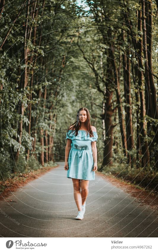 Junge 20-24 Jahre alte schlanke Brünette in einem hellblauen Sommerkleid tanzt auf der Straße zum Rhythmus der Musik. Unverfälschtes Porträt eines ganz normalen Menschen, der Bewegung und Tanz genießt. Sich selbst kennenlernen