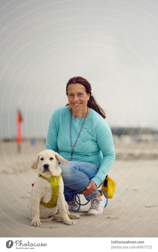 Attraktive lächelnde Frau posiert mit ihrem Welpen am Strand kniend auf dem Sand mit Kopie Raum oben Hund bezaubernd Labrador Retriever blond Sitzen