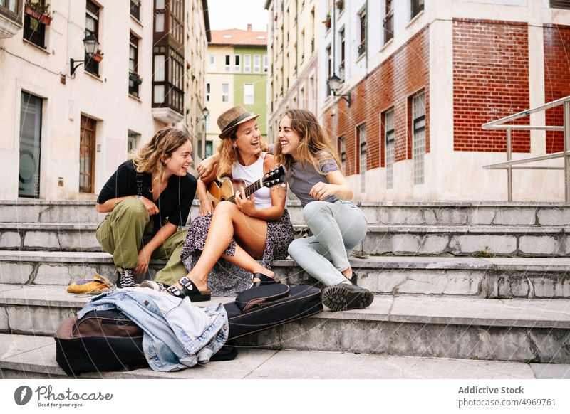 Frau mit Hut spielt Gitarre Gesellschaft von lächelnden Freunden sitti Gebäude Musik Straße Architektur Freundschaft Instrument Musical Partnerschaft