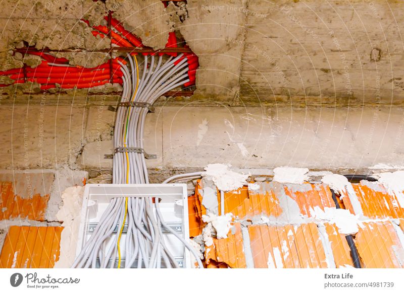 Ein Kabelstapel hängt an einem Sicherungskasten, der an der Wand eines unfertigen Gebäudes angebracht ist. Klotz Kasten Baustein Baustelle Bündel Schaltkreis
