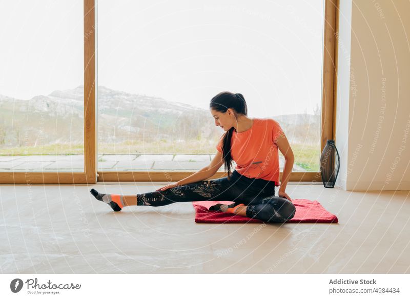 Schlanke Frau sitzt streckend im Zimmer Dame Sport erhöht Hand Sportbekleidung schlank aktiv Yoga Fenster Raum Aktivität gymnastisch Panorama Berge u. Gebirge