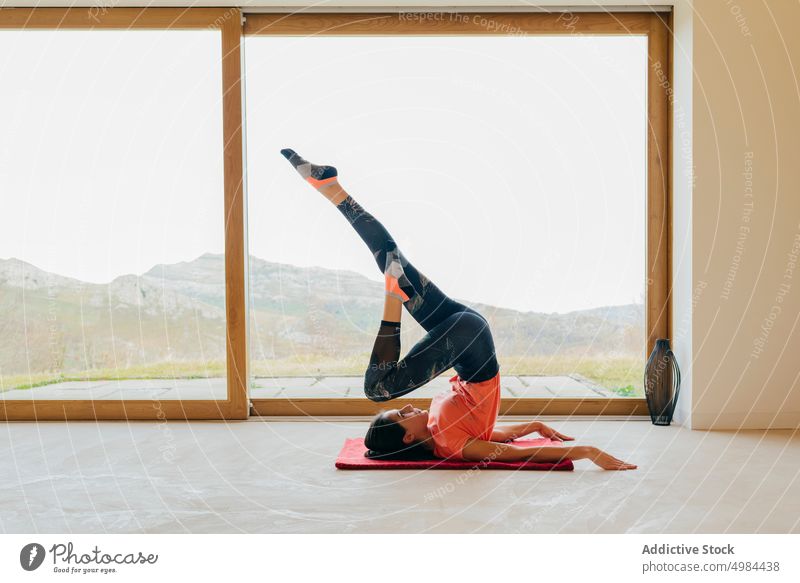 Schlanke Frau sitzt streckend im Zimmer Dame Sport erhöht Hand Sportbekleidung schlank aktiv Yoga Fenster Raum Aktivität gymnastisch Panorama Berge u. Gebirge