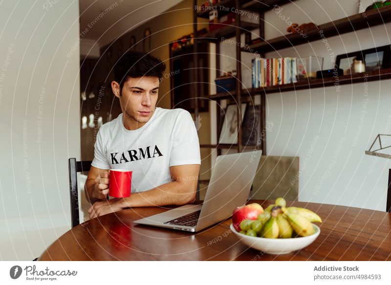 Junger Mann trinkt Kaffee und arbeitet zu Hause am Computer gutaussehend jung männlich Kaukasier heimwärts Lifestyle Morgen im Innenbereich Fokus Glück Tasse