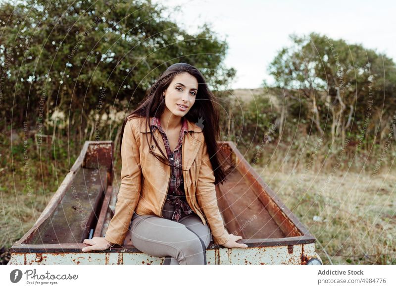 Charmante Frau sitzt auf rostigem Wagen in der Landschaft heiter ländlich Stil modern Körperhaltung Sitzen Natur trendy ruhig Außenseite gealtert allein