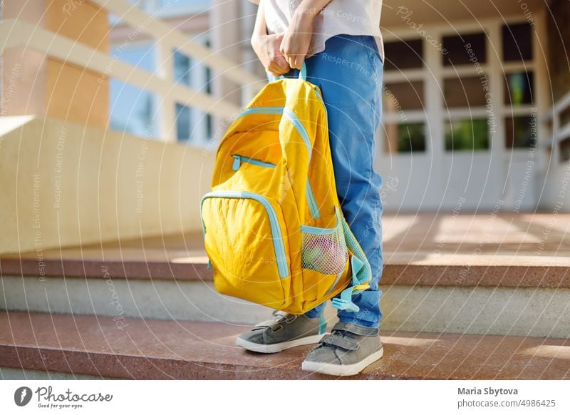 Kleiner Schüler mit einem Rucksack auf den Stufen der Treppe des Schulgebäudes. Nahaufnahme des Kindes Beine, Hände und Schultasche des Jungen auf der Treppe des Schulhauses stehend.back to school Konzept.
