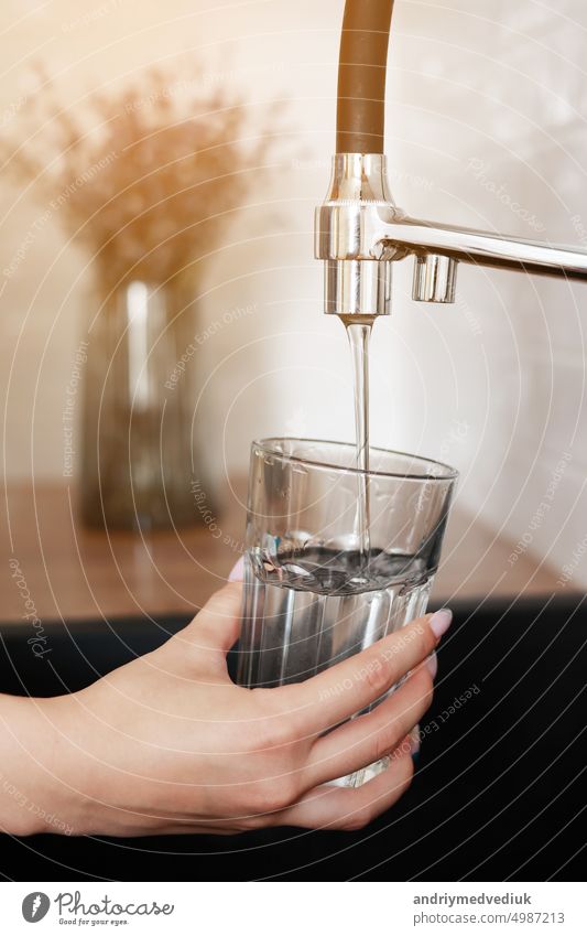 Frau füllt Trinkglas mit Leitungswasser in der Küche. Konzept der sauberen Trinkwasser Leitungswasser zu Hause. Pouring frisches Getränk. Konzept zur Überprüfung der Wasserqualität. Das Konzept der Einsparung, Probleme mit Wasser