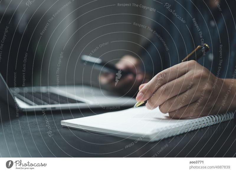 Ein Mann schreibt mit einem Stift auf einen Notizblock und ein Smartphone liegt auf dem Schreibtisch. Telefon Buch Schreibstift Büro Business Bildung Schüler