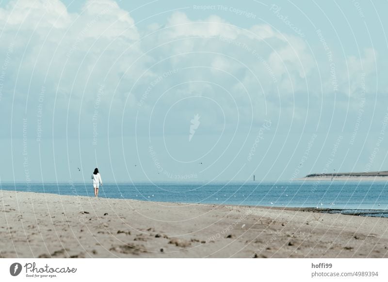 eine Spaziergängerin am Strand mit Leuchtturm und Insel im Hintergrund Frau Mensch Spaziergang Küste Nordsee Nordseestrand Ruhe entspannend Urlaub Sommer Herbst