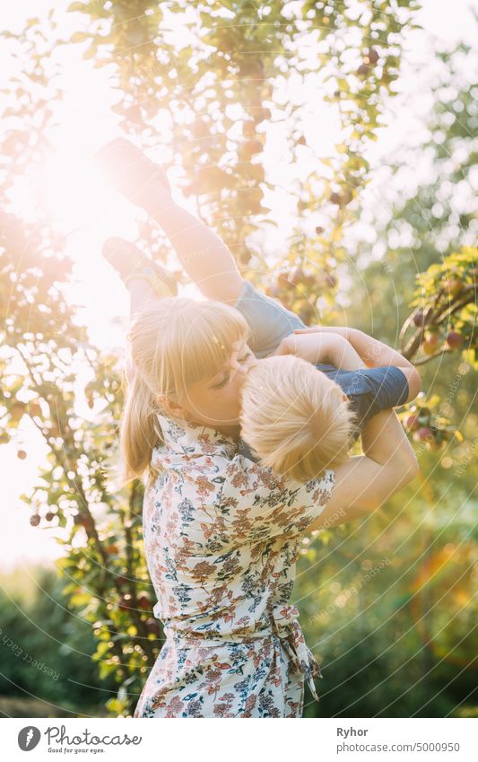 Junge Frau Mutter umarmt und küsst ihr Baby Sohn im sonnigen Garten. Outdoor Sommer Porträt schön blond Pflege Kaukasier Kind Kindheit filigran Kleid Abend