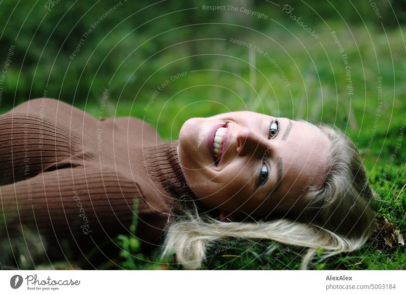 Junge, blonde Frau mit Grübchen liegt im Wald auf dem Moos und lächelt von der Seite in die Kamera junge Frau feminin schön glücklich Jugendliche Portrait