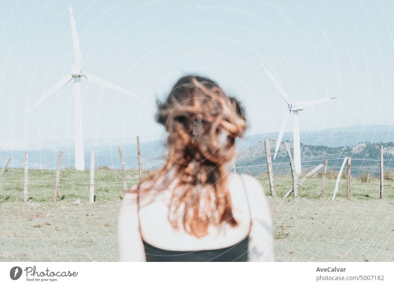 Von hinten junge Frau stehend mit Blick auf die von elektrischen Windrädern umgeben. Blowing Haar und entspannen, saubere Erde Zukunft Konzept Person Freiheit