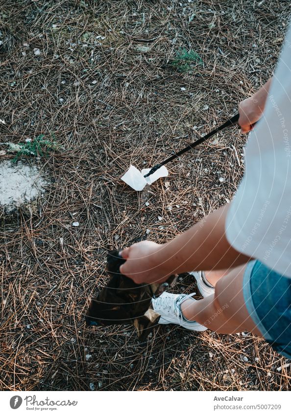 Eine junge Frau sammelt in einem schwarzen Sack im Wald zurückgelassene Abfälle ein. Plastikverschmutzung und Umweltschutz - Problem der Bettökologie und der Umweltverschmutzung durch sich lange zersetzende Abfälle