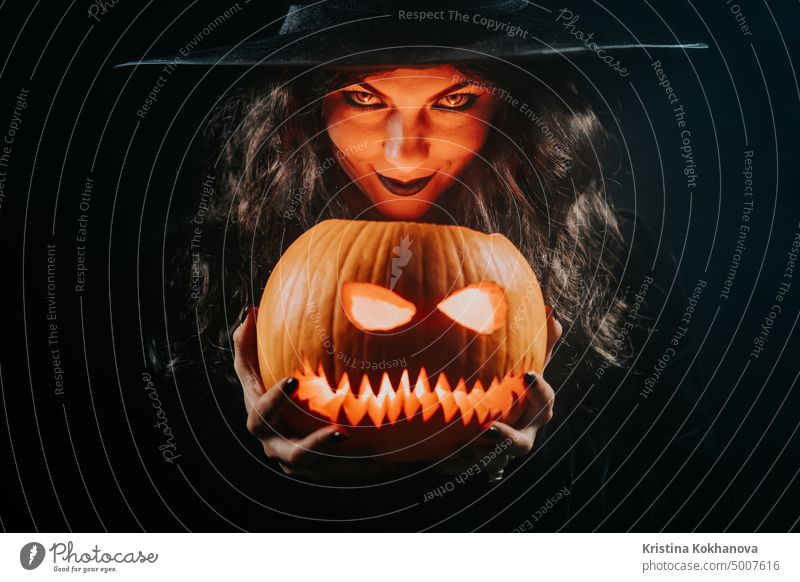 Mysteriöse schwarze Hexe mit Kürbis als Kopf der Jack-O-Lantern auf dunklem Hintergrund. Gruseliges Symbol für Halloween, Maskenkostüm, Partydekoration. Magie, klassische Hexe