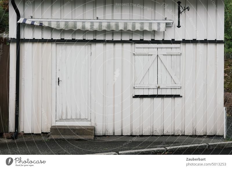 Weiße Wand eines norwegischen Holzhauses mit geschlossener Tür und Fensterläden weiß Norwegen Fensterladen verriegelt Saison Fassade Haus Gebäude
