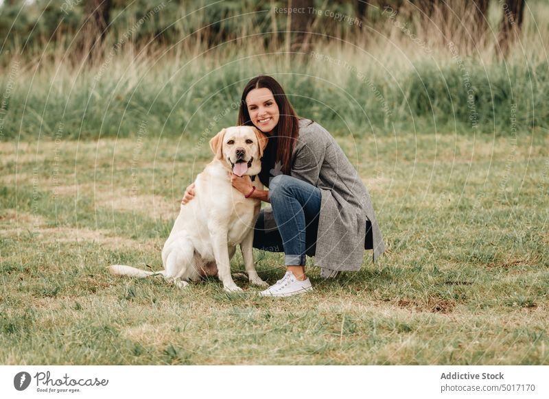 Frau umarmt fröhlichen Hund, der im Gras sitzt Park Spaß Glück umarmend Haustier Natur grün Tier Labrador Retriever freudig Zusammensein Freundschaft