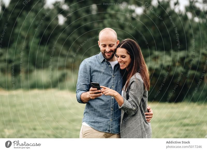 Verliebtes Paar schaut sich Fotos auf dem Handy an kuscheln Umarmung schießen Angebot Park Wiese süß Liebhaber Freizeitkleidung Liebe Romantik Zusammensein