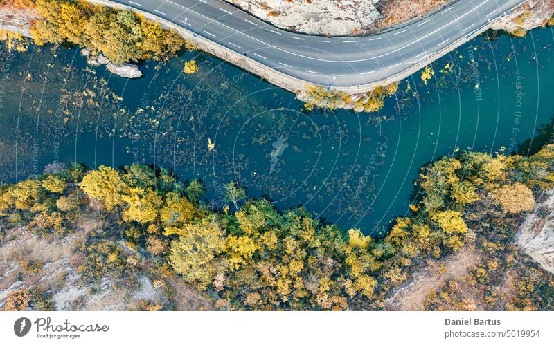 Eine Straße an einem Berghang mit Blick auf einen Fluss mit bunter Vegetation und Bäumen am Rande des Hanges. Ansicht aus dem Drohnenflug. Hintergrund Herbst