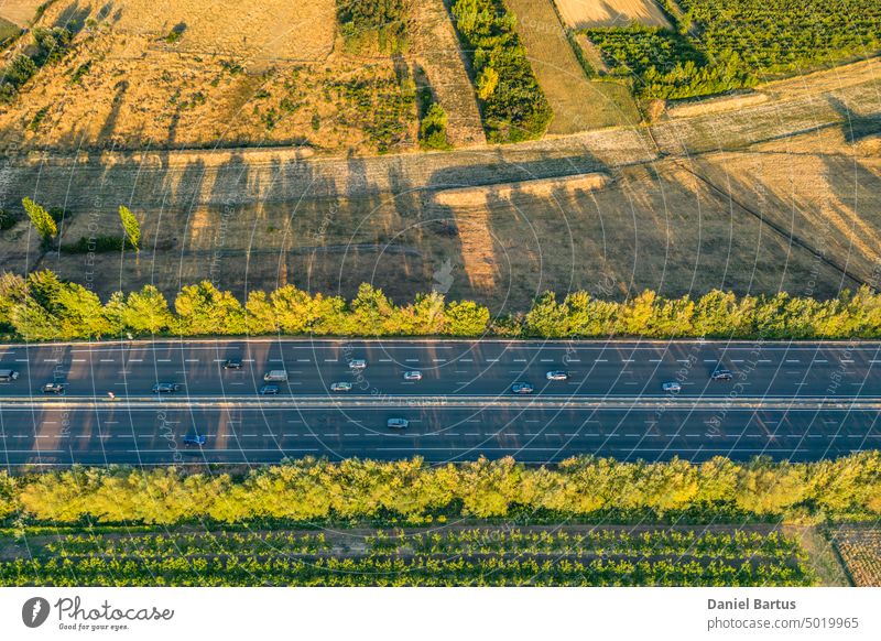 Highway aus der Vogelperspektive. Wenn die Sonne untergeht, werfen die Sonnenstrahlen schöne lange Schatten auf den Boden. Gelbe Bäume und umliegendes Ackerland