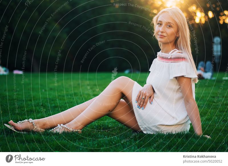 Schöne blonde Frau sitzt auf grünem Gras im Park im Sommer und schaut in die Kamera attraktiv schön Schönheit Kaukasier Mädchen Glück Lifestyle Natur im Freien