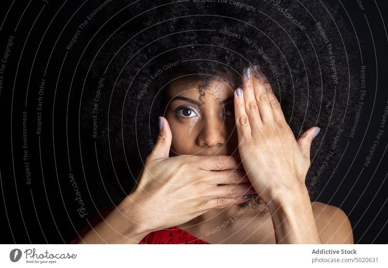 Schüchterne ethnische Frau bedeckt Gesicht auf schwarzem Hintergrund Auge abdecken Deckel Mund schüchtern feminin Tierhaut Angebot Afro-Look Porträt sanft