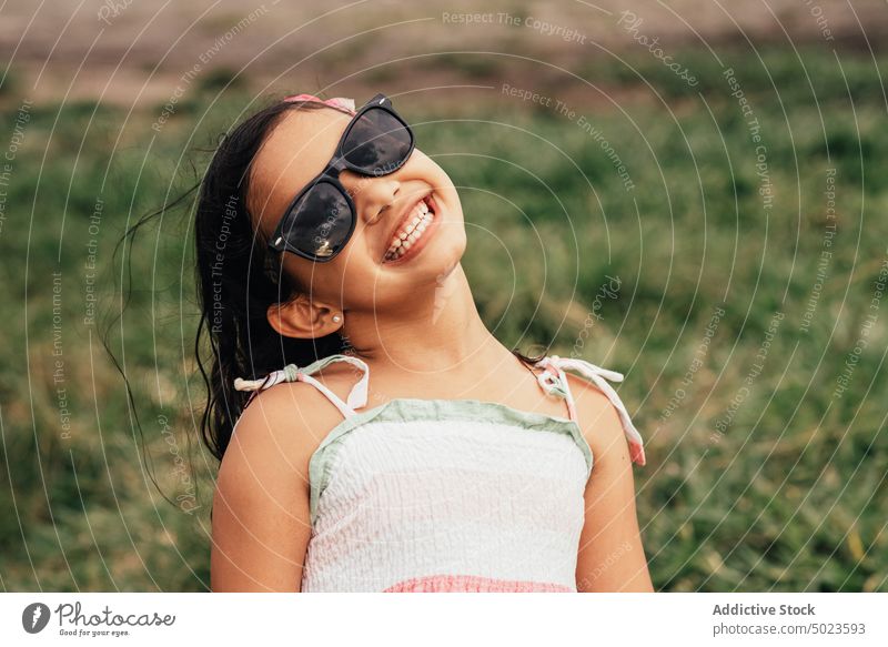 Optimistisches Mädchen mit Sonnenbrille auf einem Feld Lächeln Sommer ruhen Wochenende Stil Gras Portwein