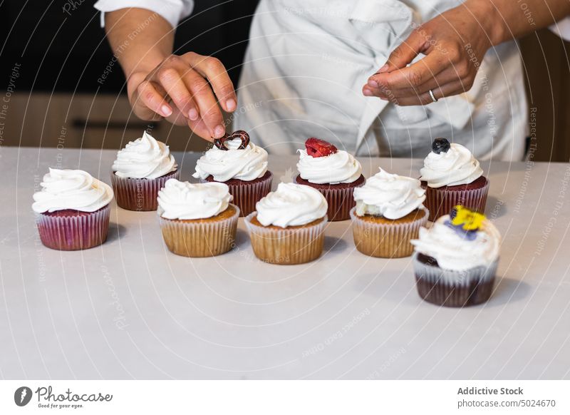 Anonymer Bäcker beim Dekorieren von Cupcakes am Tisch Bäckerei dekorieren Beeren Frau süß Dessert Veganer Küche Abfertigungsschalter Gebäck gebacken kulinarisch