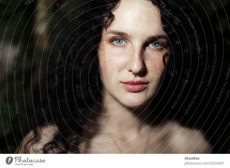 Nahes Portrait einer jungen, dunkelhaarige Frau mit Locken, hellblauen Augen und Sommersprossen - im Hintergrund ist Efeu zu sehen junge Frau brünett