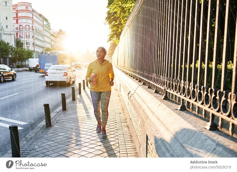 Ältere Sportlerin läuft auf der Straße laufen Sonnenaufgang Herz Fitness Training Straßenbelag Morgen Übung Frau Wellness Wohlbefinden atmen Energie Aktivität