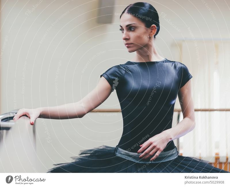 Ballerina in schwarzem Tutu und Spitzen dehnt sich an der Stange im Ballettstudio. Frau steht in der Nähe von Bar und Spiegel, die Vorbereitung für perfomance.